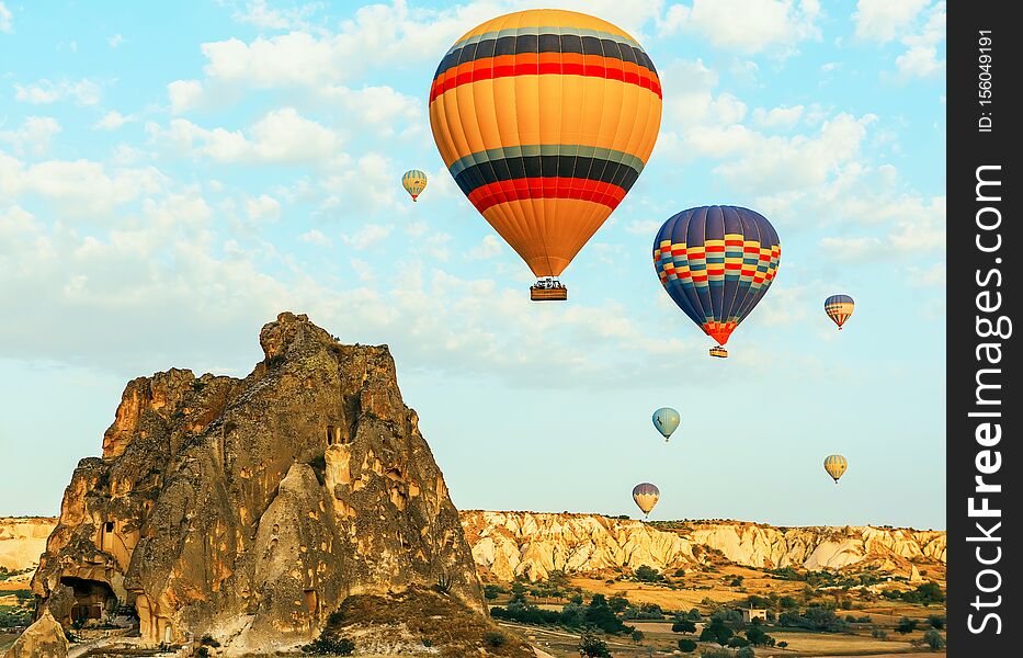 Colorful air balloons fly up into the sky at sunrise among a beautiful rocky landscape.