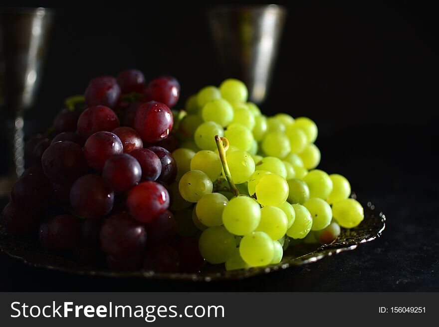 A traditional Mediterranean platter with grapes and wine on black background. A traditional Mediterranean platter with grapes and wine on black background.