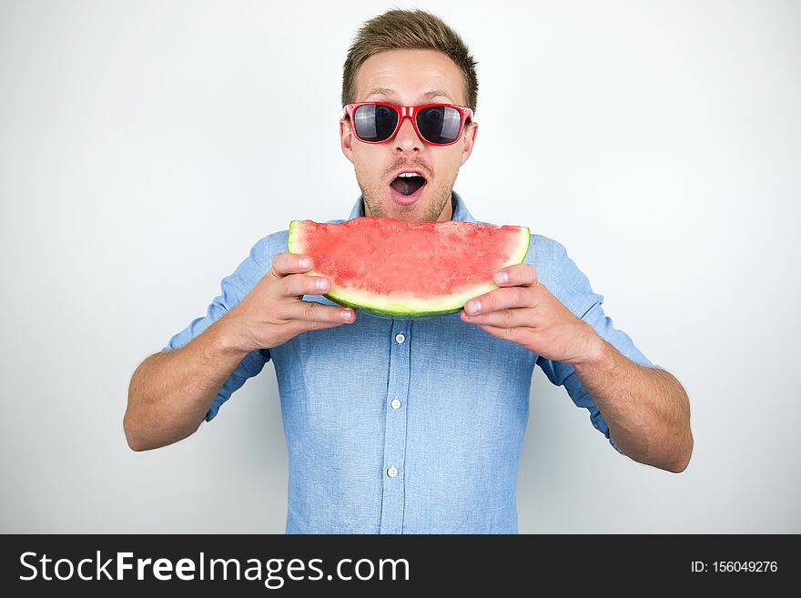 Young handsome man in red eyeglasses biting watermelon on isolated white background.