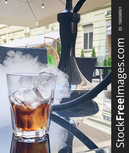Glass of cold whiskey with hookah on table.