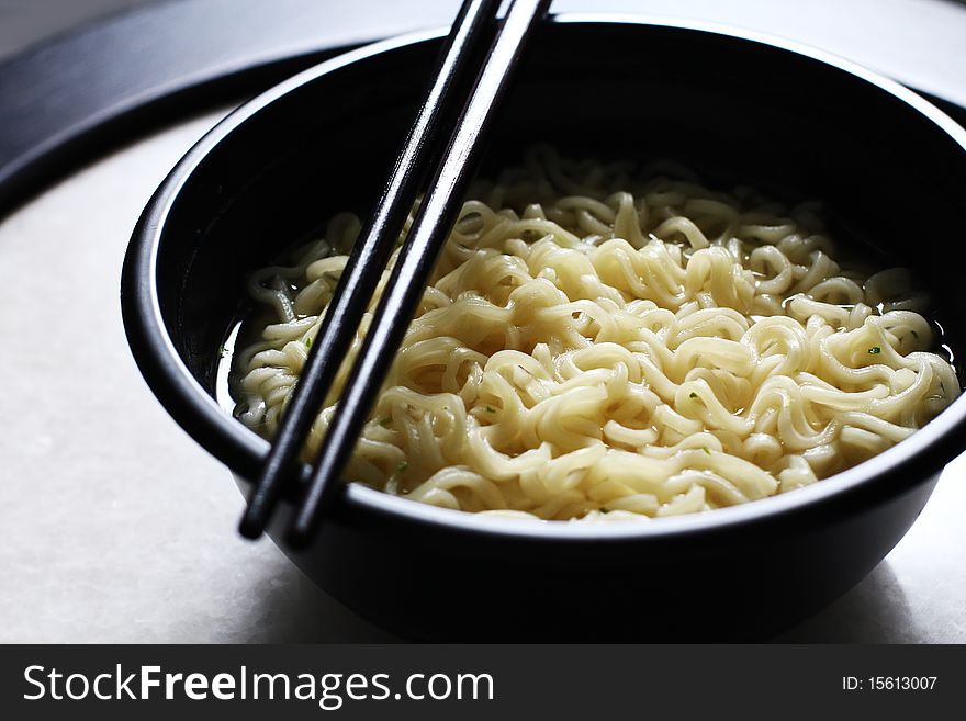 Asian noodle with chopstick served in a black bowl.