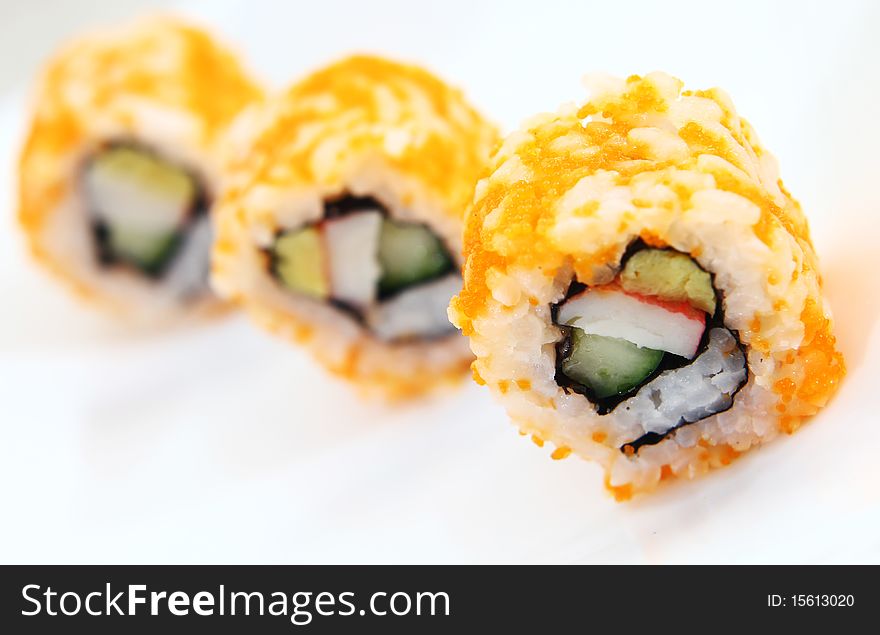 Japanese sushi covered in orange shrimp roe, arranged in single file and served on a white platter.