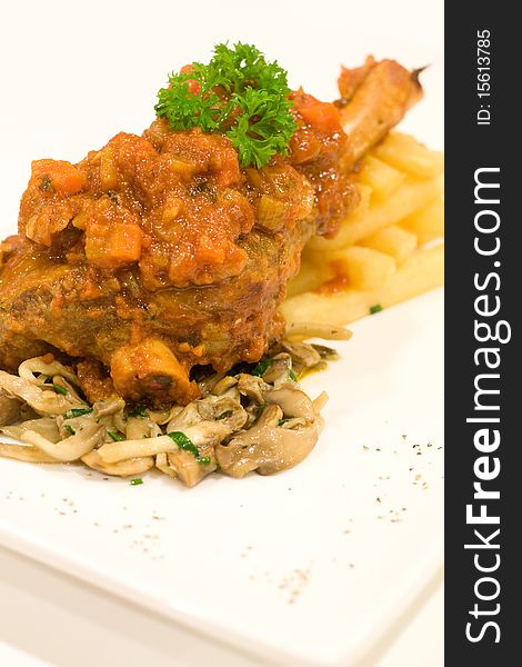 Grilled Lamb Shank served with tomato gravy, french fries, placed on white plate