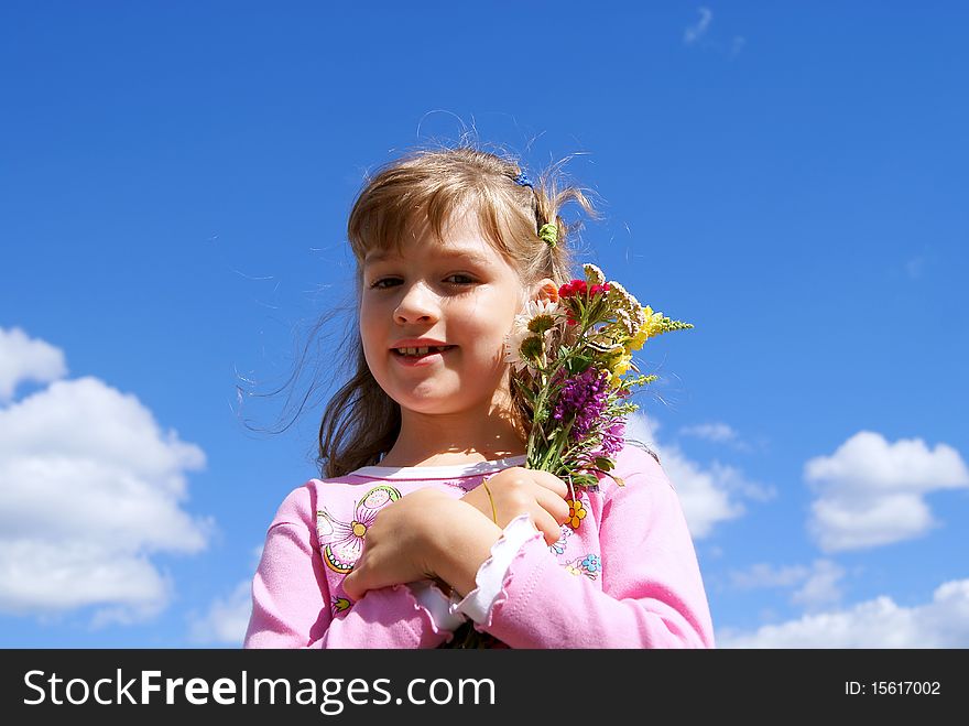 The beautiful girl stands against the sky with a bouquet of wild flowers. The beautiful girl stands against the sky with a bouquet of wild flowers