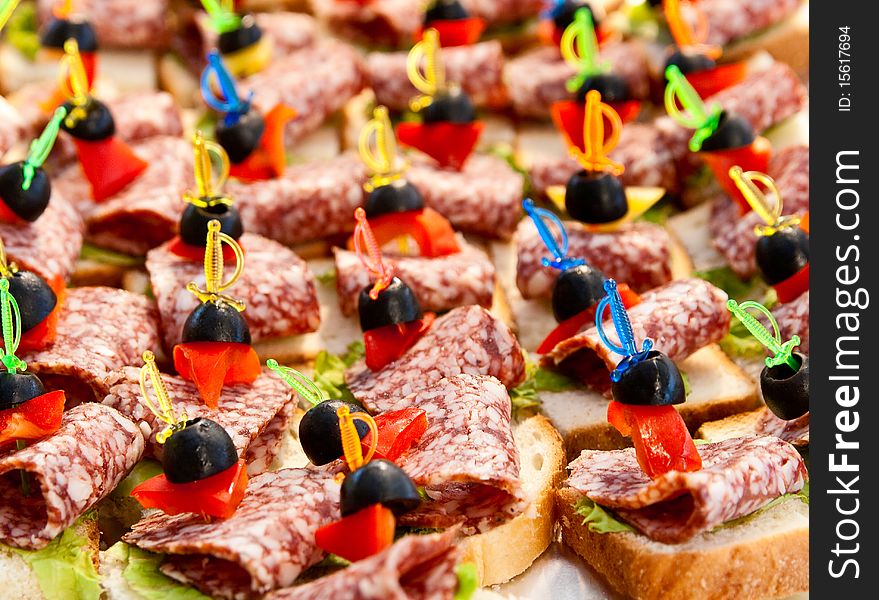 Many small sandwiches with salami and olives on skewers. Many small sandwiches with salami and olives on skewers.
