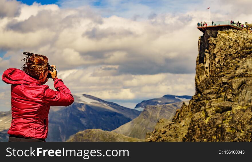 Tourism vacation and travel picture. Female tourist taking photo with camera, enjoying mountains landscape at windy day. Dalsnibba Plateau viewpoint in the distance, Norway. Tourism vacation and travel picture. Female tourist taking photo with camera, enjoying mountains landscape at windy day. Dalsnibba Plateau viewpoint in the distance, Norway
