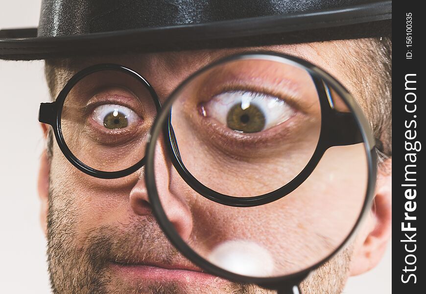 Funny adult guy wearig weird eyeglasses investigating something using magnifying glass making his eye looking big. Funny adult guy wearig weird eyeglasses investigating something using magnifying glass making his eye looking big