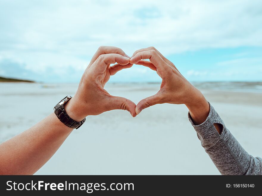 hands of a woman and a man forming a heart shape against a cloudy sky