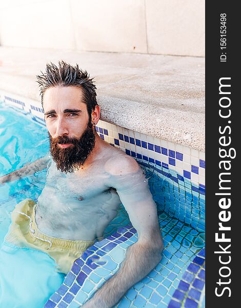 Portrait of a relaxed young man with a beard sitting in the pool. Holiday concept