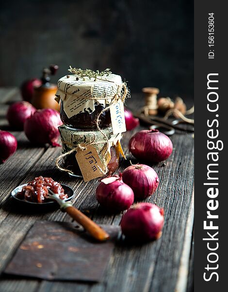 Homemade tasty canned onion red jam, marmalade, confiture, chutney in two glass jars on rustic wooden table with red onion and bowl with jam on fork. Selective focus