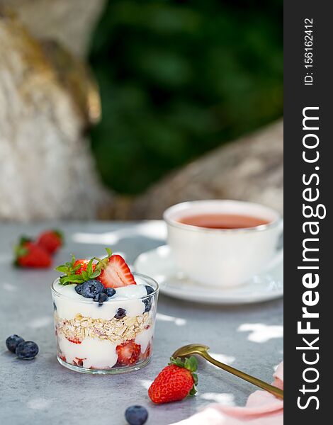 Granola in glass with berries and tea cup in garden. Concept of super food breakfast