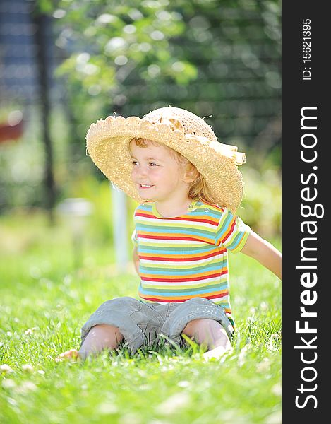 Little girl in straw hat sitting on green grass
