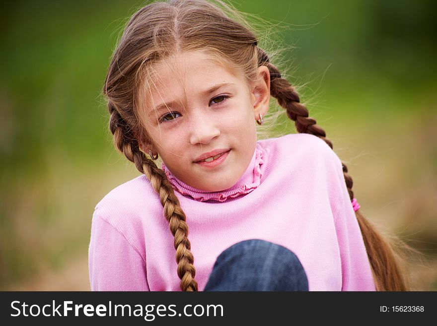 Portrait of little girl with pigtails smiling at the camera against  background of green