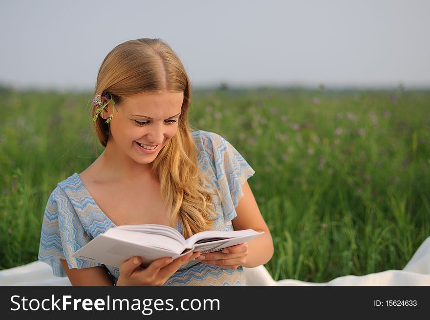 Young girl sitting on green grass and reading a book