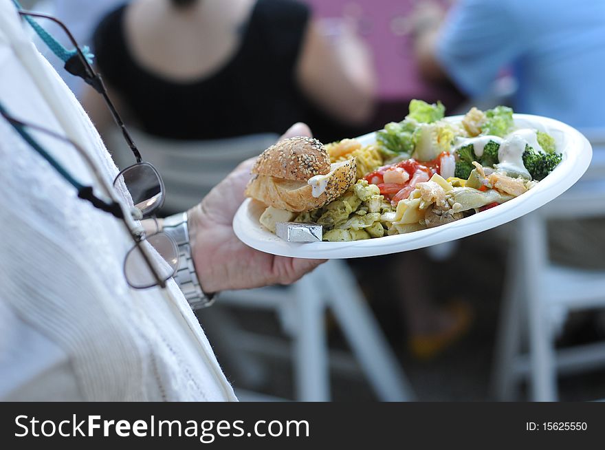 A man walks back to his table with his paper plate filled with food at a party. A man walks back to his table with his paper plate filled with food at a party.