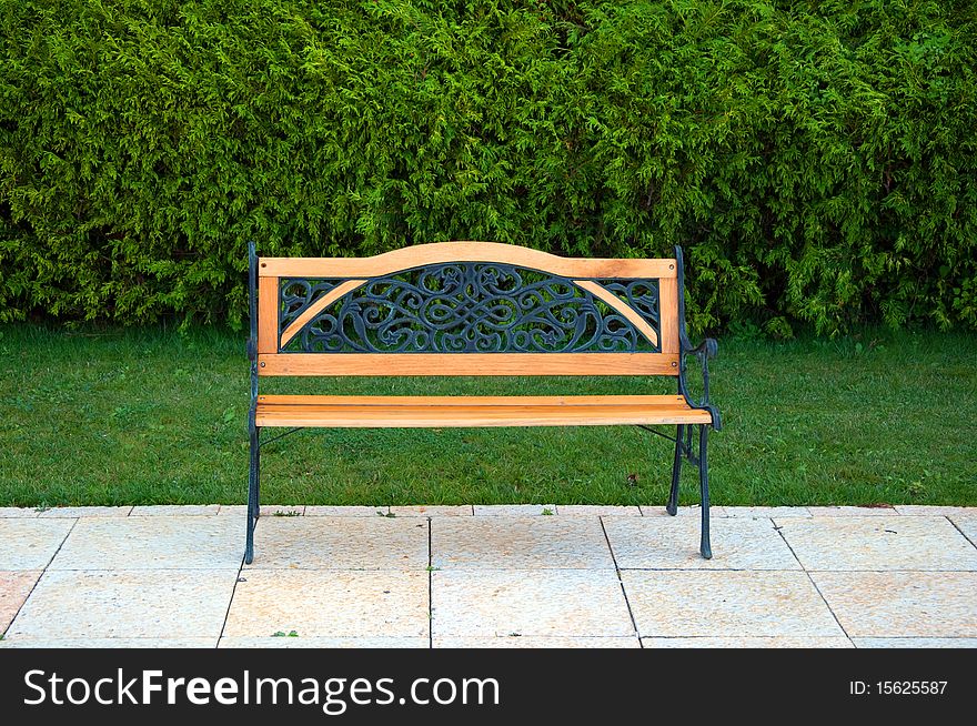 Nice little cast metal and wooden bench in front of the green grass and cypress plantations. Nice little cast metal and wooden bench in front of the green grass and cypress plantations