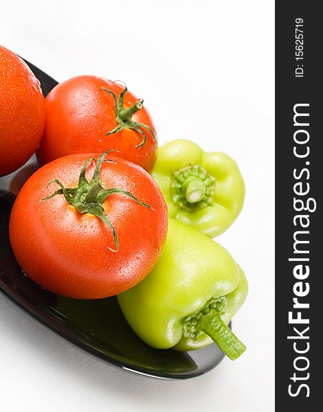 Fresh tomatoes and peppers washed and placed in a black ceramic plate isolated on white background