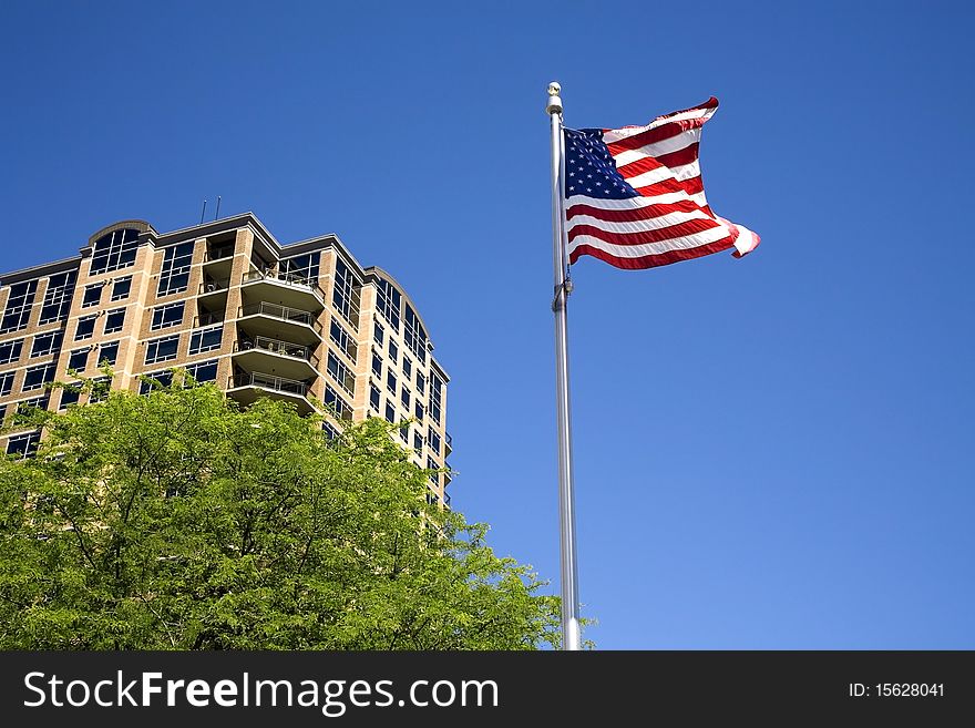 A US flag waves in the wind by a building partly behind a tree. A US flag waves in the wind by a building partly behind a tree.