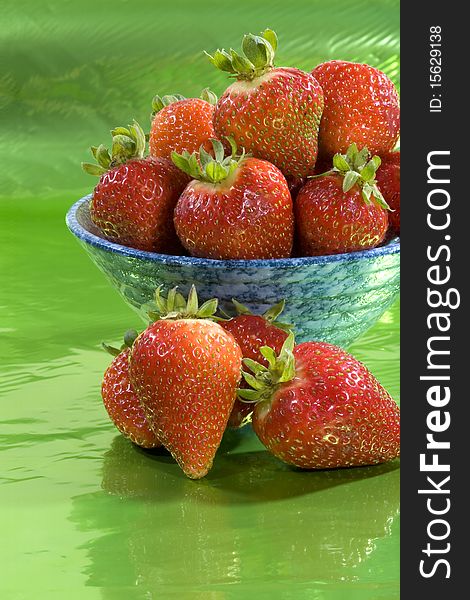 Red strawberries in a bowl against a green background. Red strawberries in a bowl against a green background.