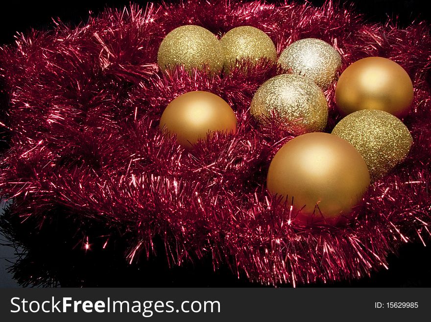 Eight gold christmas decoration balls on red tinsel on black background