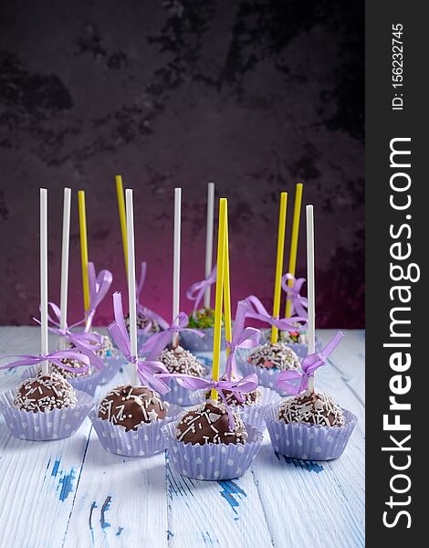 Cake pops coated chocolate with sprinkling on wooden table table on dark background with copy space