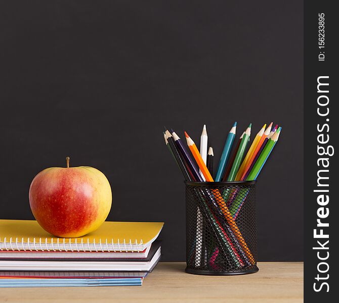 Close up of back to school supplies with apple in front of chalkboard, copy space