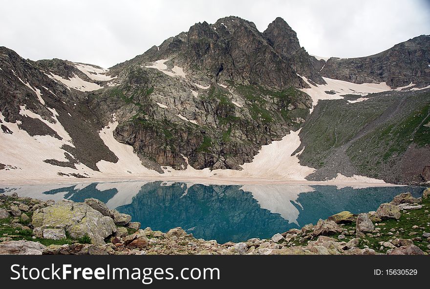 Reflection of snow and rocks in the deep blue highland lake. Wheather is cloudy.