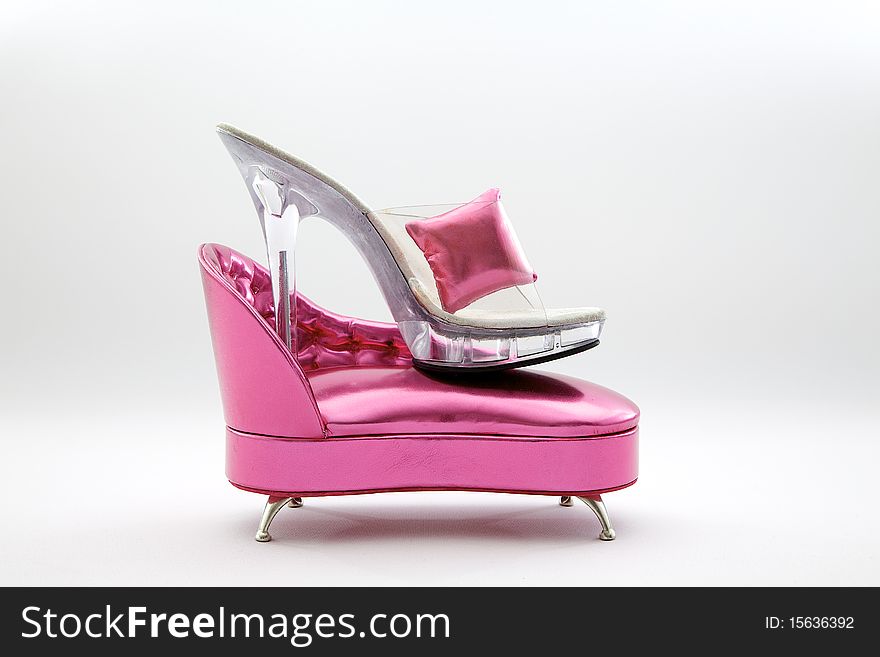Silver high heel resting over a miniature pink sofa isolated with white background. Silver high heel resting over a miniature pink sofa isolated with white background