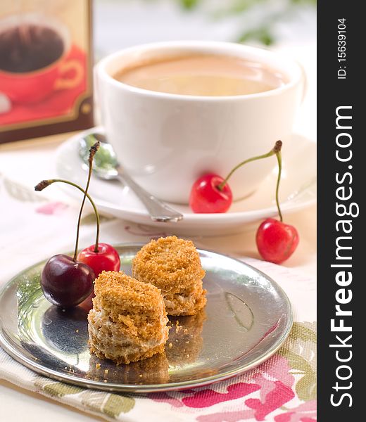 Two small honey cakes on a plate with cherry and coffee in background. Two small honey cakes on a plate with cherry and coffee in background.