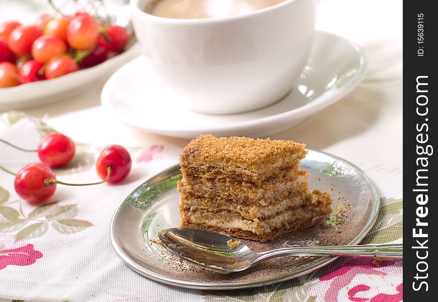 Slice of honey cake on a plate with spoon and coffee in background. Slice of honey cake on a plate with spoon and coffee in background.