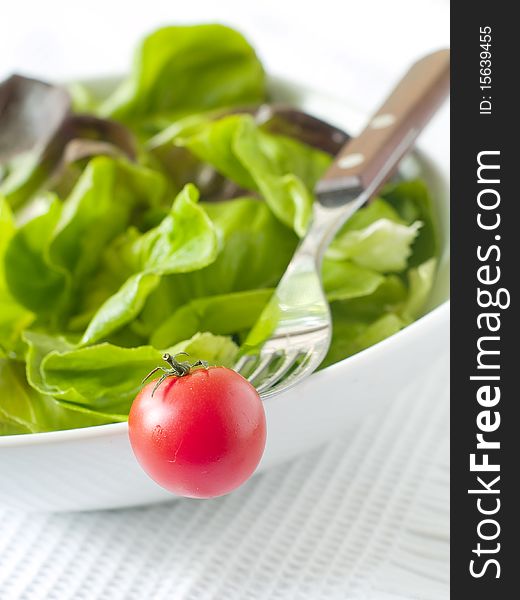 Fork with tomato and bowl of lettuce in background. Fork with tomato and bowl of lettuce in background