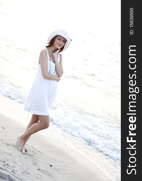 Beautiful young red-haired girl in hat on the beach of Black Sea. Sea and sunlight is on background. Beautiful young red-haired girl in hat on the beach of Black Sea. Sea and sunlight is on background.