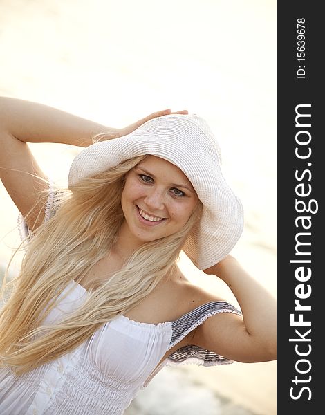Beautiful young blonde girl in hat on the beach of Black Sea. Sea and sunlight is on background.