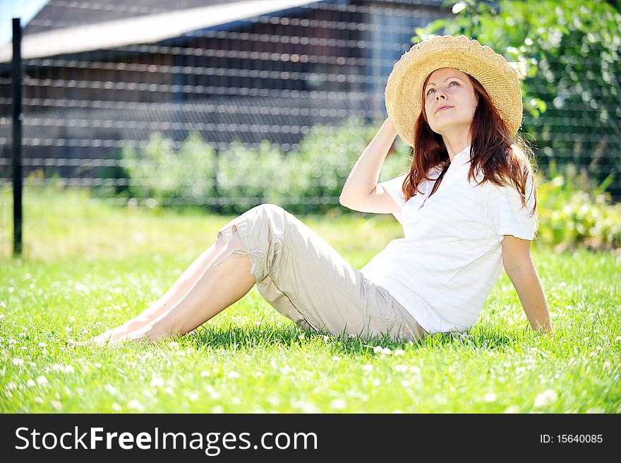 Young woman in straw hat  sitting on green grass