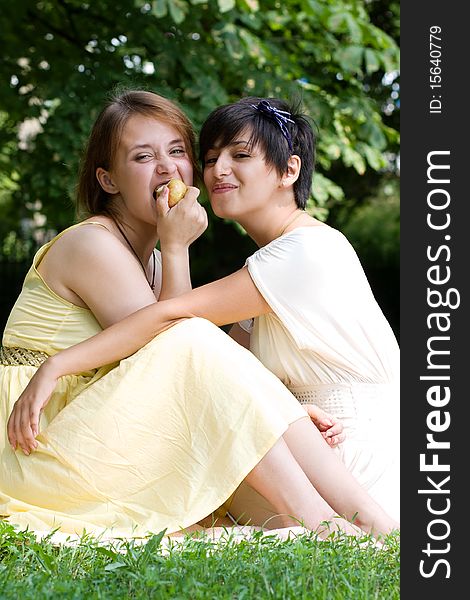 Two girls eating an apple outdoors smiling