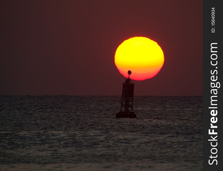 Buoy swaying in ocean in front of sunrise