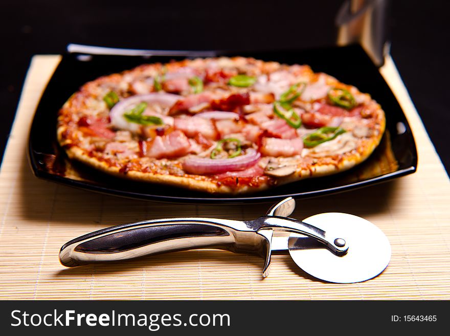 Delicious pizza with everything on it and pizza cutter in focus