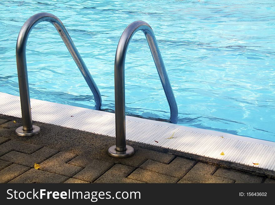 Stainless steel pool ladder goes down into blue water