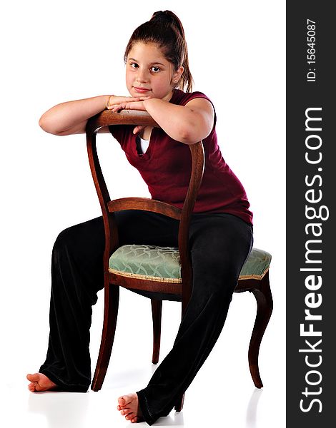 An attractive preteen girl sitting backwards in an antique chair. Isolated on white.