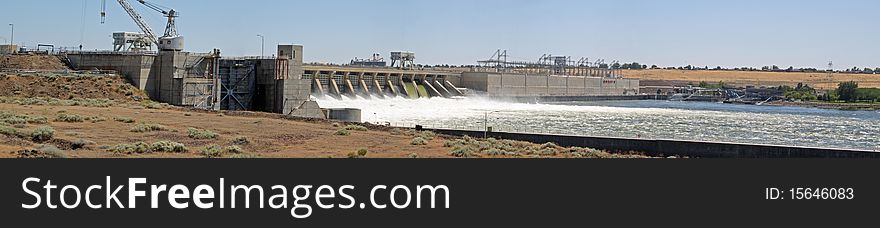 Wide panorama of a concrete dam, with water flowing over the spillway. Wide panorama of a concrete dam, with water flowing over the spillway