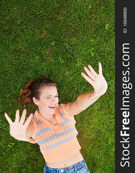 Attractive teenager lying down on green grass with hands rised up to the air. Attractive teenager lying down on green grass with hands rised up to the air