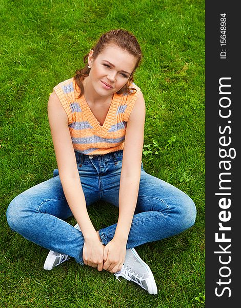 Attractive teenage girl sitting on green lawn in casual clothes looking at camera with smile. Attractive teenage girl sitting on green lawn in casual clothes looking at camera with smile