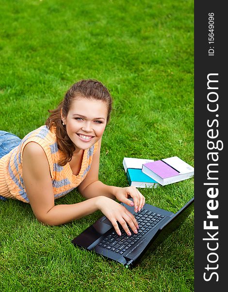 Pretty caucasian teenager lying down on green grass with laptop and books. Pretty caucasian teenager lying down on green grass with laptop and books