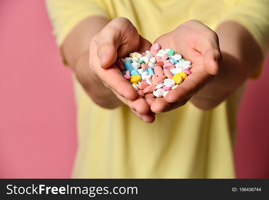 A handsome man in a yellow T-shirt on a pink background, holding pills in his hand