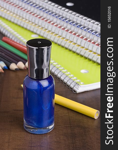 Blue nail polish standing in front of colored pencils and a stack of notebooks.