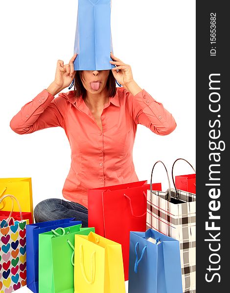 Brunette woman sitting in the middle of colored shopping-bags with one on her head. Brunette woman sitting in the middle of colored shopping-bags with one on her head