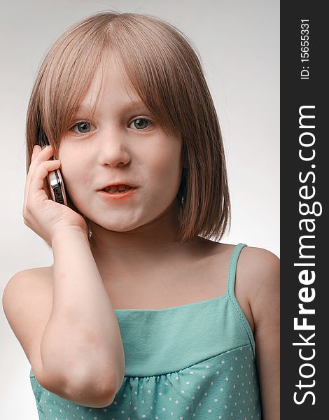 The girl calls by phone. Age of the girl of 5 years. Phone modern, cellular, with the metal case. A background neutral, gray