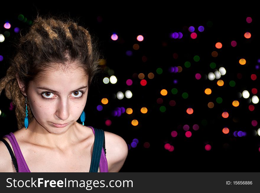 Portrait of attractive young woman on a colorful night lights background.  Big eyes, dreadlocks, blue earrings.