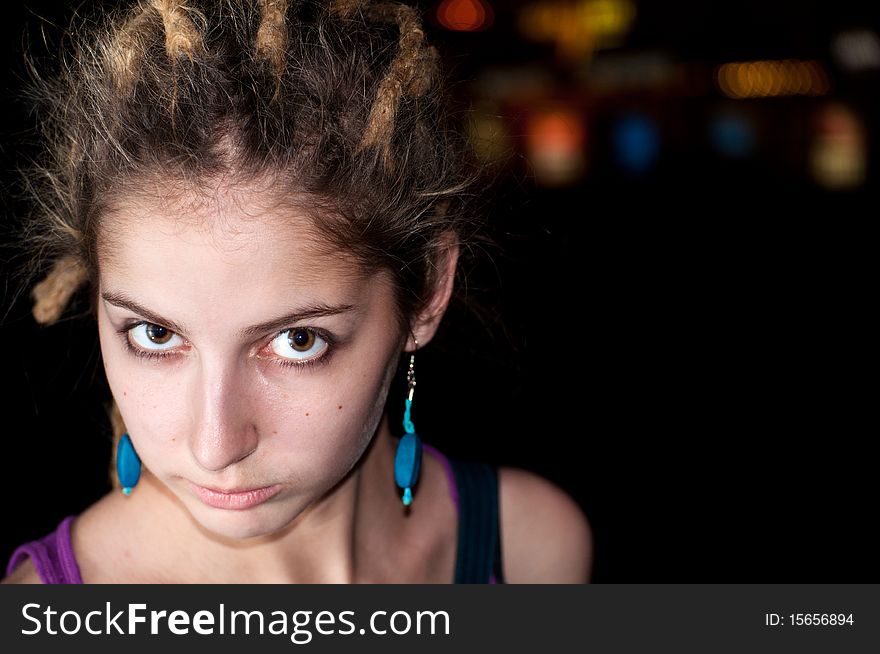 Portrait of attractive young woman on a colorful night lights background.  Big eyes, dreadlocks, blue earrings.