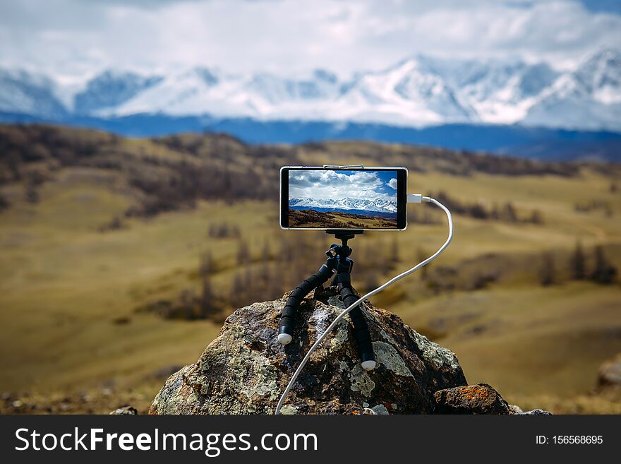 Smartphone on tripod mounted on stone in front of  stunning view of the snow-capped peaks. Image is focused on display